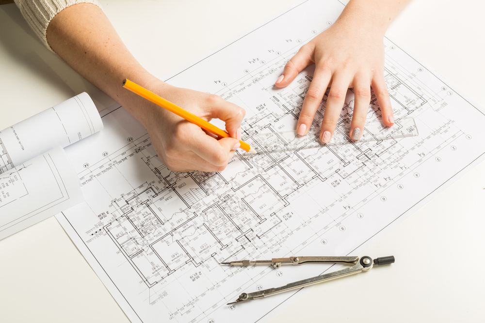 Hands holding a pencil and ruler over a blueprint