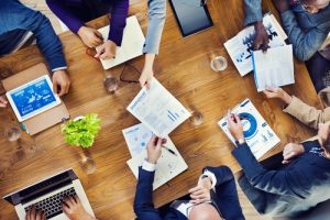 Workers sharing office reports around a wooden conference table