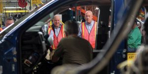 Workers observe as a car is assembled on the GM assembly line